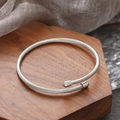 Elegantes, gedrehtes Armreif-Armband in Silber auf einem Holzuntergrund.