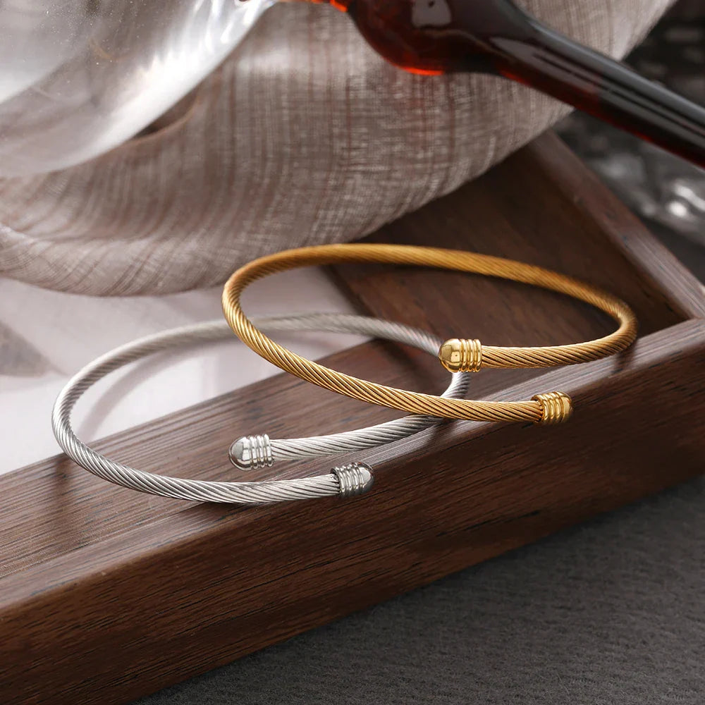 Elegantes gedrehtes Armreif-Armband in Gold und Silber auf einem Holztablett.